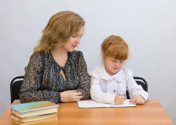 Meisje met haar moeder schrijft aan de tafel met oefening boeken en schoolboeken — Stockfoto