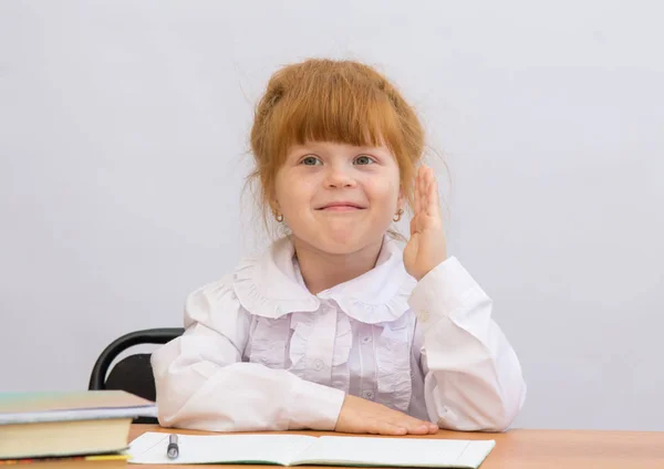 Het kleine meisje zit op een school-Bureau, het verhogen van zijn hand te beantwoorden — Stockfoto
