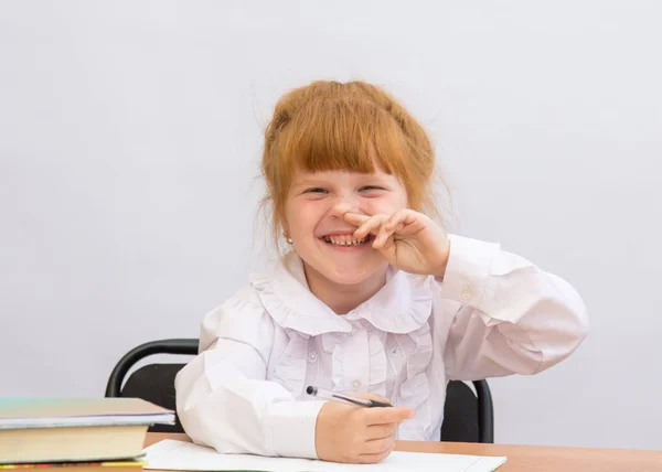 Niña en el escritorio se ríe alegremente, sosteniendo su nariz —  Fotos de Stock