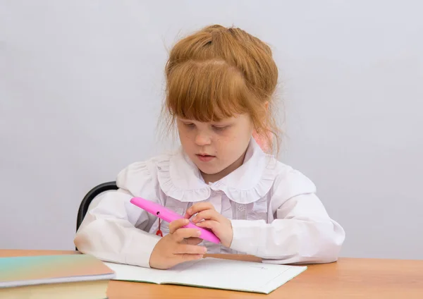 La niña en la mesa sosteniendo un celular rosa —  Fotos de Stock