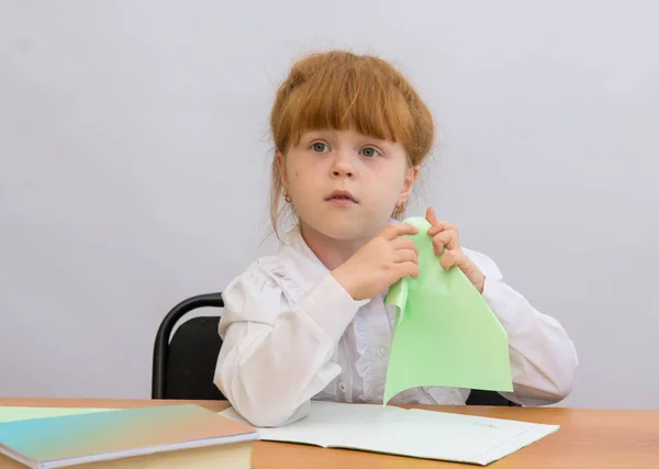 Het meisje aan de tafel houden een papieren vliegtuigje — Stockfoto