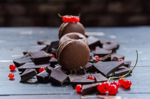 Çikolata renkli macarons gri ahşap üzerinde. Kırmızı kuş üzümü bir dekor. Yakın çekim.