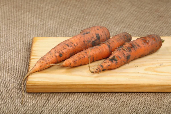 Tres zanahorias crudas en tablero de madera sobre lienzo —  Fotos de Stock