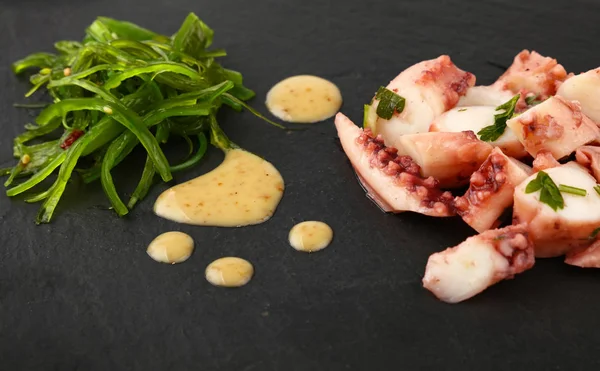 Octopus arm slices and seaweed salad on black — Stock Photo, Image