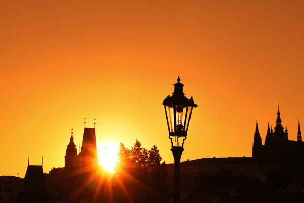 Sunset backlit silhouettes of street lamp post and roofs of cityscape skyline at Charles Bridge in Prague, Czech Republic
