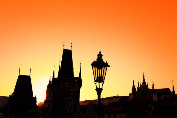 Sunset backlit silhouettes of street lamp post and roofs of cityscape skyline at Charles Bridge in Prague, Czech Republic
