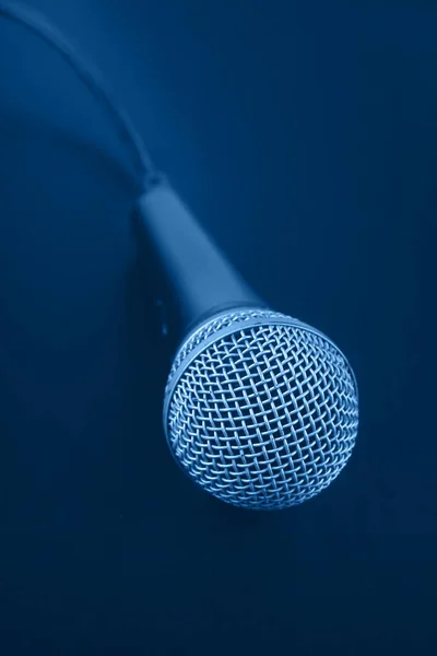 Close up classic wired vocal microphone with cable over dark blue background, high angle view, personal perspective