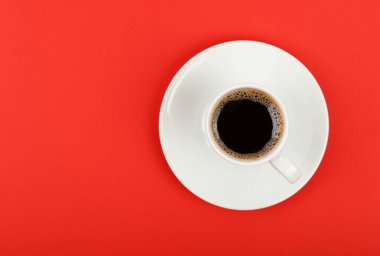 Bir fincan dolusu siyah kahveyi kırmızı arkaplanda, üst manzaranın üstünde, çay tabağının üzerinde kapayın.