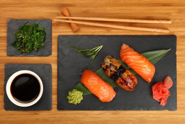 Üç nigiri sushi setini somon ve yılan balığı ile kapatın. Tahta masanın üzerinde siyah tahta tahta tahtada servis edilir. Üst manzarası yüksektir.