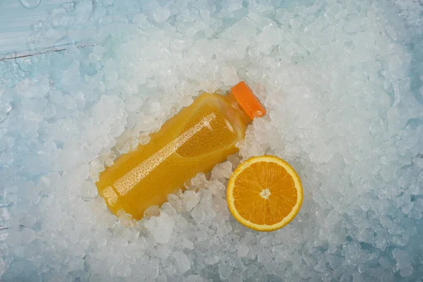 Close up one plastic PET bottle of fresh orange juice and cut half orange slice over background of crushed ice, elevated high angle view, directly above