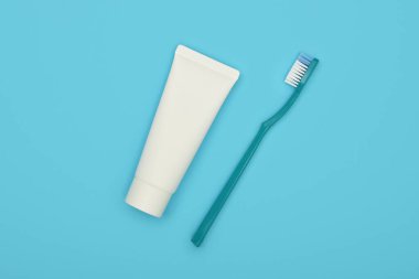 Mavi zemin üzerinde beyaz bir diş macunu tüpü ve plastik diş fırçası kapatın, düz zemin, yüksek üst görünüm, tam üzerinde