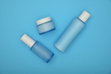 Üç adet kozmetik cilt bakım kremi, losyon ve tonik şişesini pastel mavi arka plan üzerine kapatın. Üst görünüm, doğrudan üst görüntünün üzerine.