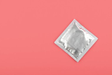 Pastel pembe arka plan üzerinde bir adet gümüş prezervatif paketini fotokopi alanı ile kapatın, yüksek açılı görünüm, tam yukarıda.