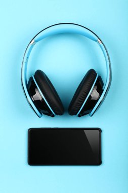 Close up modern wireless plastic blue headphones with big cushions and black mobile phone on table, elevated top view, directly above clipart