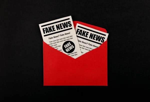 Close up brown paper mail envelope with FAKE NEWS newspapers over black background with copy space, elevated top view, directly above