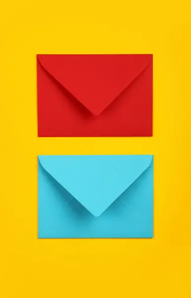 鮮やかな黄色の背景の上に2つの閉じた空白のパステルブルーと赤の紙の封筒 フラットレイ — ストック写真