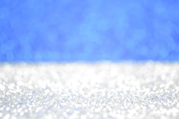 White sparkle snow flakes on blue sky background. Shimmer glitter defocused bokeh wallpaper
