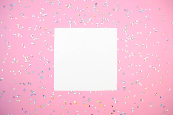 Empty white square paper card and holographic stars confetti flat lay on pink mock up