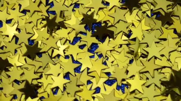 Gold yellow confetti shines at different angles, shake off fallen stars of classic blue glitter background — стоковое видео