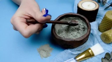 Mavi arka planda maske hazırlamak için gri tıbbi kozmetik kil. Malzemeleri elle karıştır.