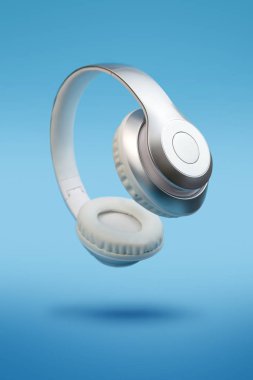 Mavi arka planda gümüş metalik beyaz kablosuz kulaklıklar var. Uçan müzik aleti konsepti