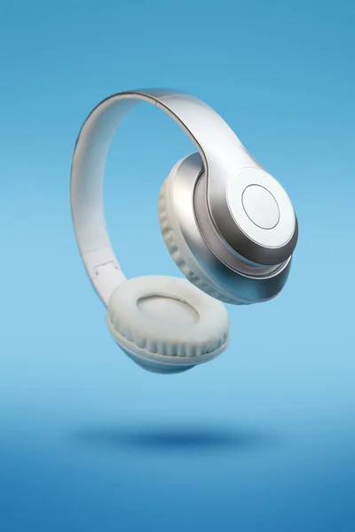Mavi arka planda gümüş metalik beyaz kablosuz kulaklıklar var. Uçan müzik aleti konsepti