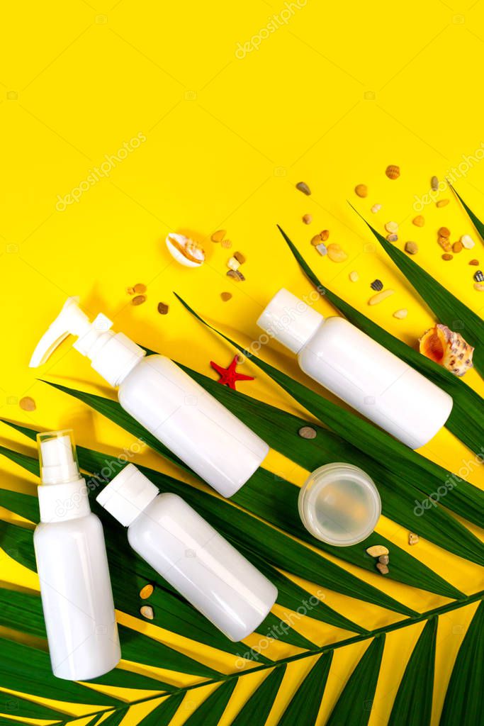 Summer trevel size cosmetics flat lay on yellow background. Sample bottle airplane kit. Travel concept. Palm leaf, seashells, sea banner