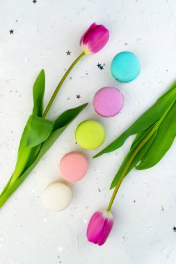 Parlak gri arka planda laleler, çiçekler ve badem kurabiyeleri. Düz Yat. Bahar çiçeği konsepti. Tatil, doğum günü Fransız tatlısı.