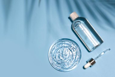 Antibakteriyel, hyaluron jeli şişesi, pipet ve mavi arka planda şeffaf kozmetik serumu lekesi. Virüs koruması ya da kozmetik konsepti. Güneş kremi. Düz konsept, kopyalama alanı