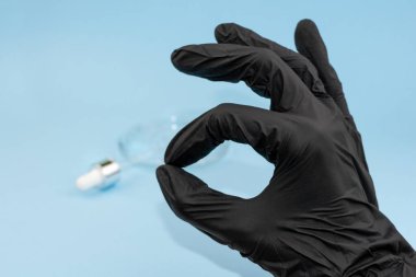 Tamam işareti. Siyah lateks eldiven verin. Antibakteriyel, hyaluron jeli şeffaf kozmetik serumu lekesi, mavi arka planda pipet. Virüs koruması ya da kozmetik konsepti. Tanı testini temizle, düzelt