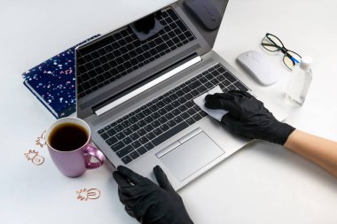 Siyah lateks eldivenli iki kadın eli antibakteriyel ıslak bezle bilgisayarı siliyor. Ofis aleti dezenfekte edildi. Laptop, antiseptik virüs koruma sağlık konsepti