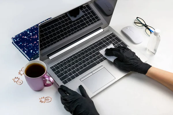 Two women\'s hands in black latex gloves wipe a computer with an antibacterial wet cloth. Office gadget disinfection at work top view. Laptop, antiseptic virus protection health care concept