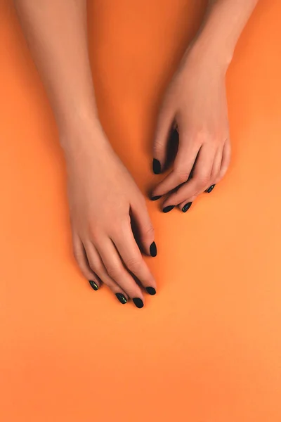 Womans hands with perfect black matte manicure with holographic metallic rainbow design on sunny orange