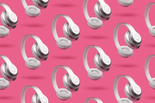 Silver metallic white wireless headphones in the air on light bright pink background. Seamless pattern. Trendy minimal music device flying levitation antigravity concept of gadget.