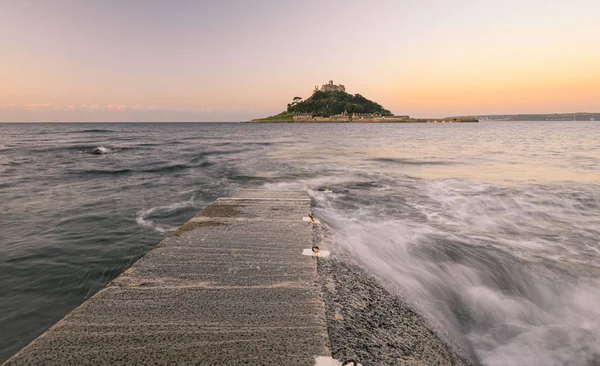 İngiltere, Cornwall, Penzance yakınlarındaki Marazion 'da bir gelgit adası olan St Michael' s Mount 'ta gün doğumu. Ada, orta gelgitle alçak su arasında geçilebilen granit yerleşimlerden oluşan insan yapımı bir geçitle bağlantılı..