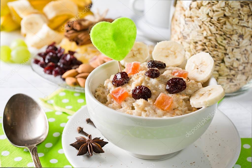  Oatmeal porridge with dried fruits, cranberries, bananas and spices. Jar of oatmeal on background. Arranged on white background.