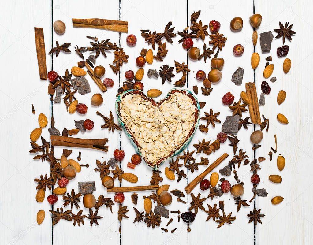 Background made of various types of spices. Centrally in the frame clay bowl in the shape of a heart.