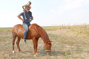 Küçük yakışıklı sevimli oğlu ve sahada kırmızı atı ile güneş gözlüğü moda adam.