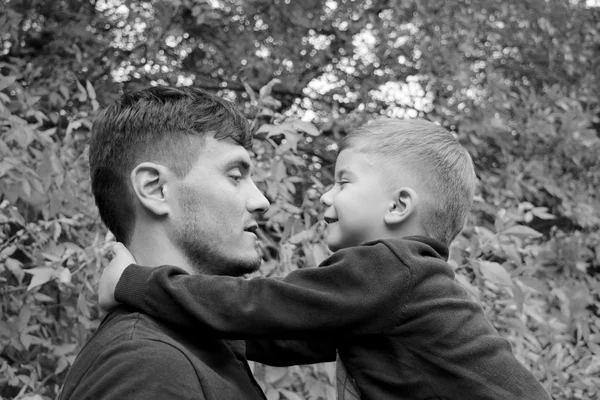 Padre sostiene a su hijo en sus brazos, padre e hijo jugando juntos al aire libre en el bosque — Foto de Stock