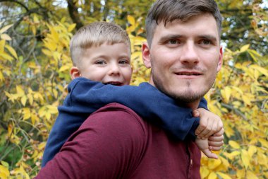 Açık havada ormanda sırtında sevimli yakışıklı küçük oğlu güçlü baba tutar