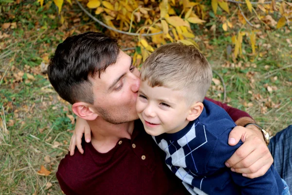 Father kiss and holds his son in his arms, outdoors — Stock Photo, Image