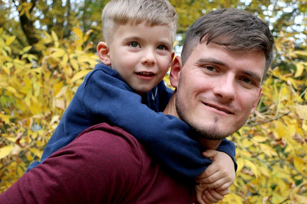 El padre fuerte sostiene a su pequeño hijo guapo lindo en su espalda al aire libre en el bosque — Foto de Stock