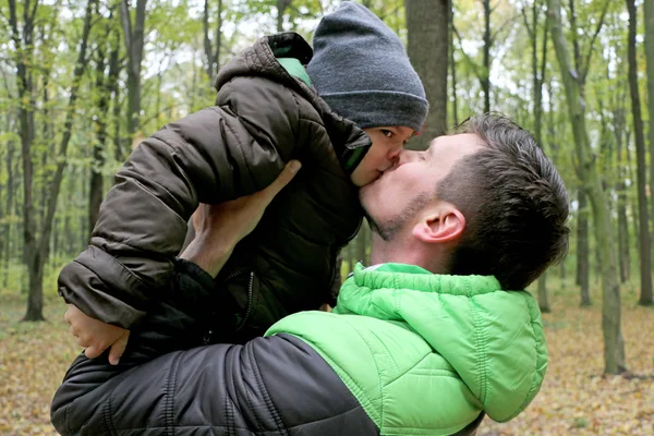 父亲抱着和亲吻他的小可爱聪明的儿子在森林里的自然 — 图库照片