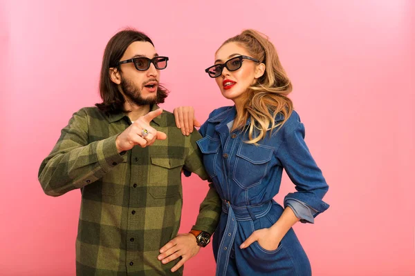 Surprised people showing each other something interesting and wonderful. Man open his mouth and put finger up. Wearing green checkered shirt and sunglasses. Woman with red lips in jeans suit