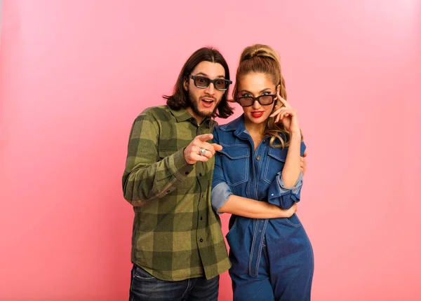 Loving people are going to the cinema, already put on the cinema glasses and choosing what movie they want to watch. Young man with beard wearing green shirt, lady in blue jeans suit, red lips