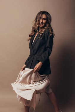 Komik kız çıldırıyor ve modern açık renk elbise ve siyah ceketle tek başına dans ediyor. Uzun kıvırcık saç stili ve güzel yüzünde parlak bir makyaj. Giysileri tutarak ve sallayarak.