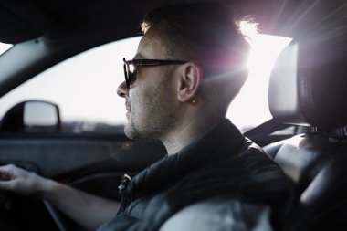 Arabasını süren ciddi yakışıklı bir adam, uzak şehre giden uzun bir yol. Ceket ve güneş gözlüğü takıyordu. İnanılmaz deri koltuklar bu yolculuğu daha rahat kılıyor. Radyoda çalan favori müzik.
