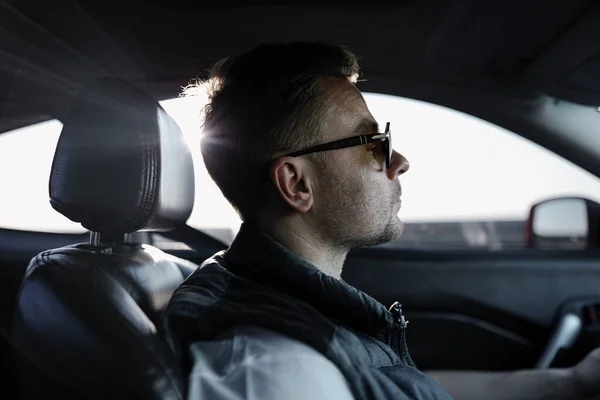 Man driving a car. Sitting on the comfortable leather sits. Mirror on the side door to see cars behind. Sunglasses on the face protects from sun rays. Long and wonderful trip.
