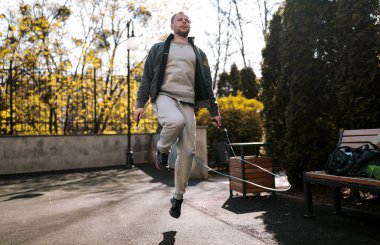 Genç bir adam spor sahasında halatla atlıyor. Rahat spor ayakkabıları, pantolonları ve ceketleri vardı. Sağlıklı ve enerjik. Etrafta yeşil ağaçlar, sabahları temiz hava. Ekipman 