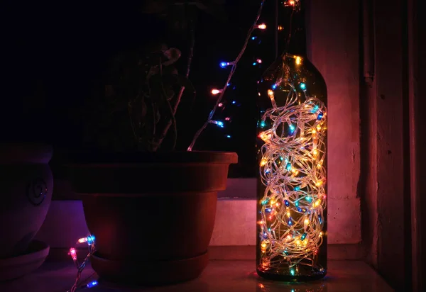 Guirnaldas de colores en la botella contra la ventana. bombillas atmosféricas —  Fotos de Stock